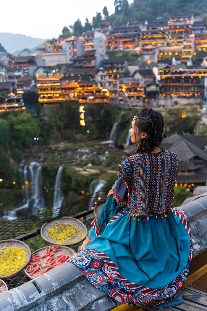 Viajera con vestimenta tradicional disfrutando de la vista panorámica de la antigua ciudad de Fenghuang, uno de los destinos turísticos más emblemáticos de China.