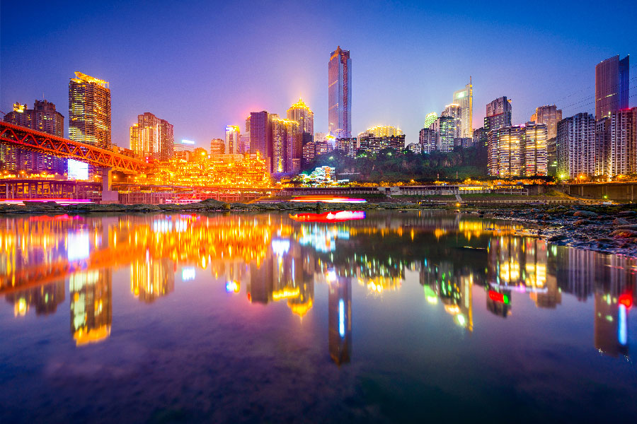 Vista nocturna del skyline de Chongqing con rascacielos iluminados y el reflejo de las luces sobre el río Yangtsé.