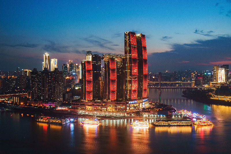 Vista panorámica del distrito financiero de Chongqing con modernos rascacielos y cruceros navegando por el río Yangtsé al anochecer.